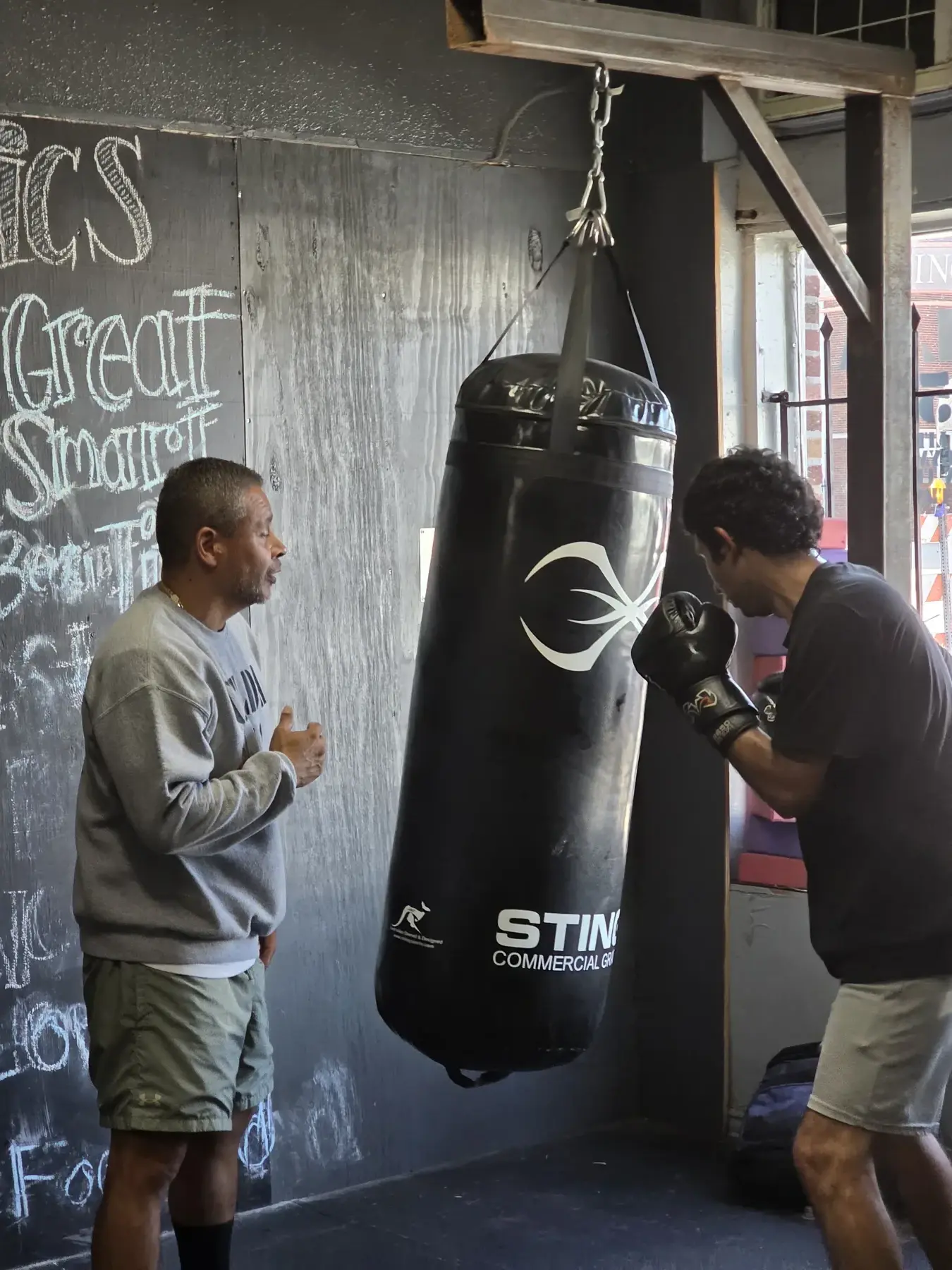 A Celda 151 coach gives focused instruction beside a heavy bag
